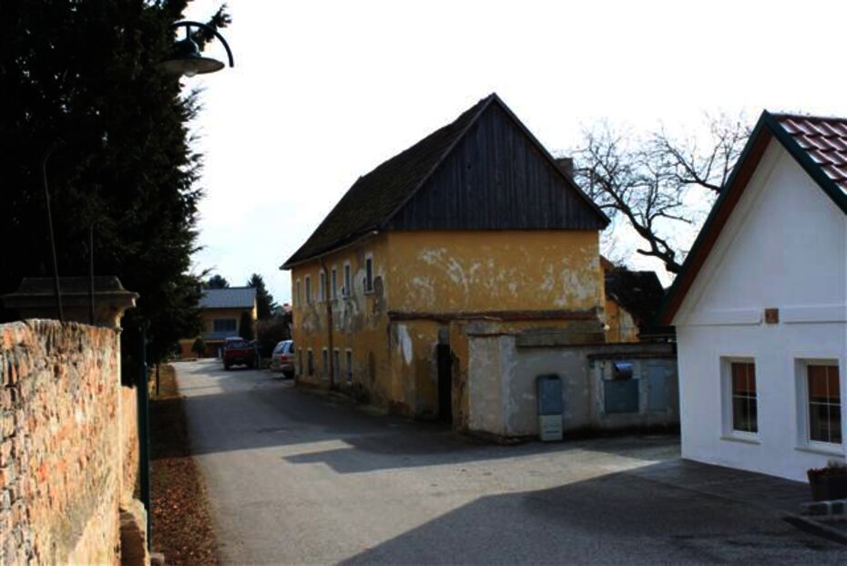 Thürnthal, ehemalige Taverne im Jahr 2012 (Bildmitte) - zweistöckiges Gebäude mit Schopfwalmdach und Zwerchgiebel. Links ist die Parkmauer mit der vermauerten Einfahrt zum Schloss Thürnthal zu sehen. [Foto: Archiv Leuthner]